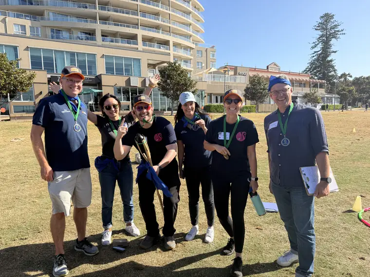Six people wearing medals on a sunny lawn at a team event