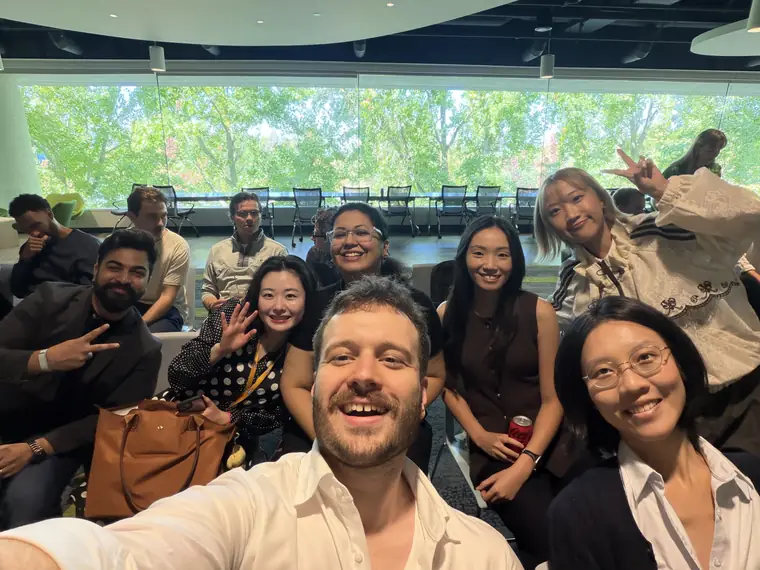 A selfie with a group of colleagues in a bright room with tall windows and trees outside